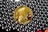 A gold-colored coin with a profile of a warrior wearing a helmet, labeled with '2014' and 'ONE BITCOIN', is surrounded by shiny, metallic beads.