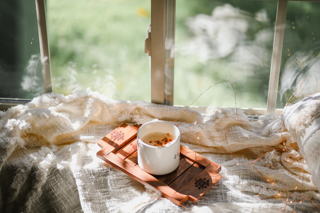 Une tasse de thé sur un plateau, posée sur un plaid près d'une fenêtre