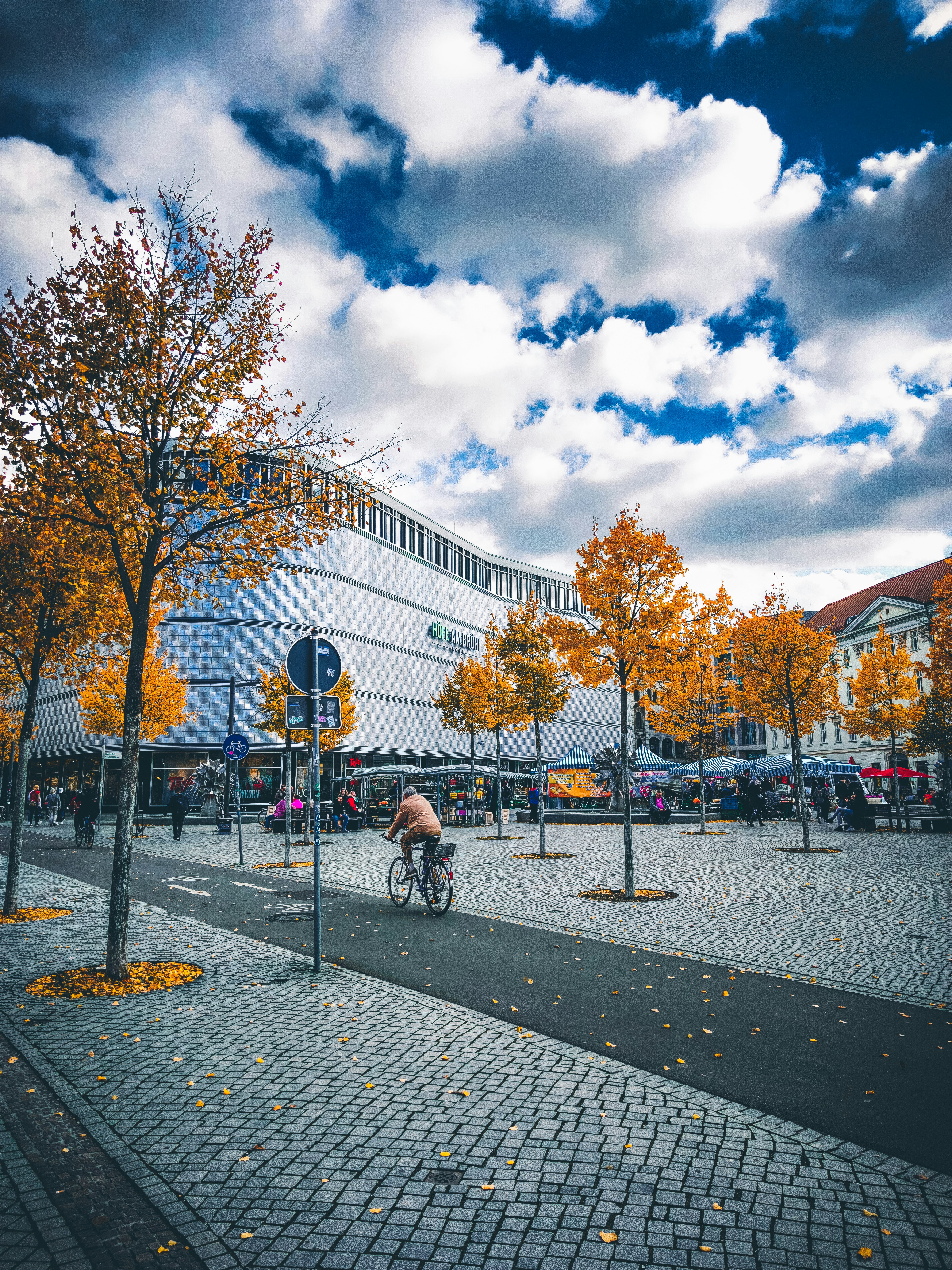 Menschen, die auf dem Park mit Bäumen und Laternenpfählen unter weißen Wolken und blauem Himmel während