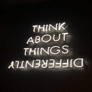 Neon sign displaying the phrase 'THINK ABOUT THINGS DIFFERENTLY' in bright white against a dark background.