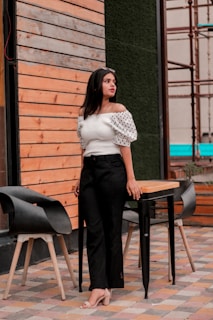 woman in white shirt and black pants standing beside brown wooden table