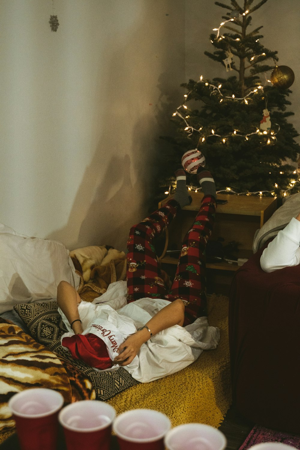 person in white shirt lying on bed beside green christmas tree
