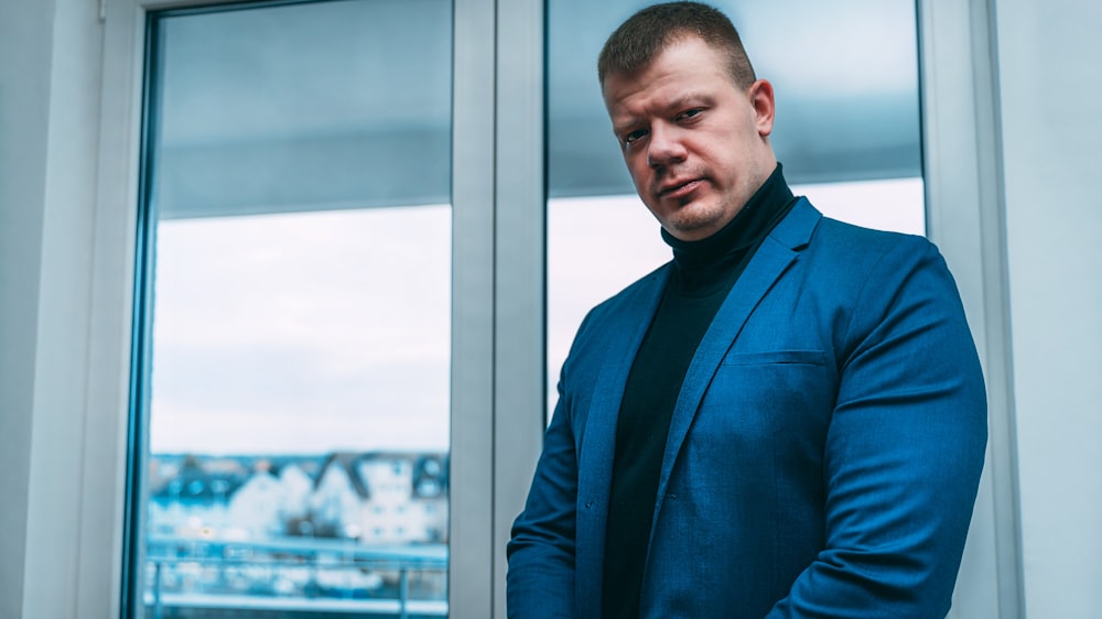 man in blue suit jacket standing beside glass window