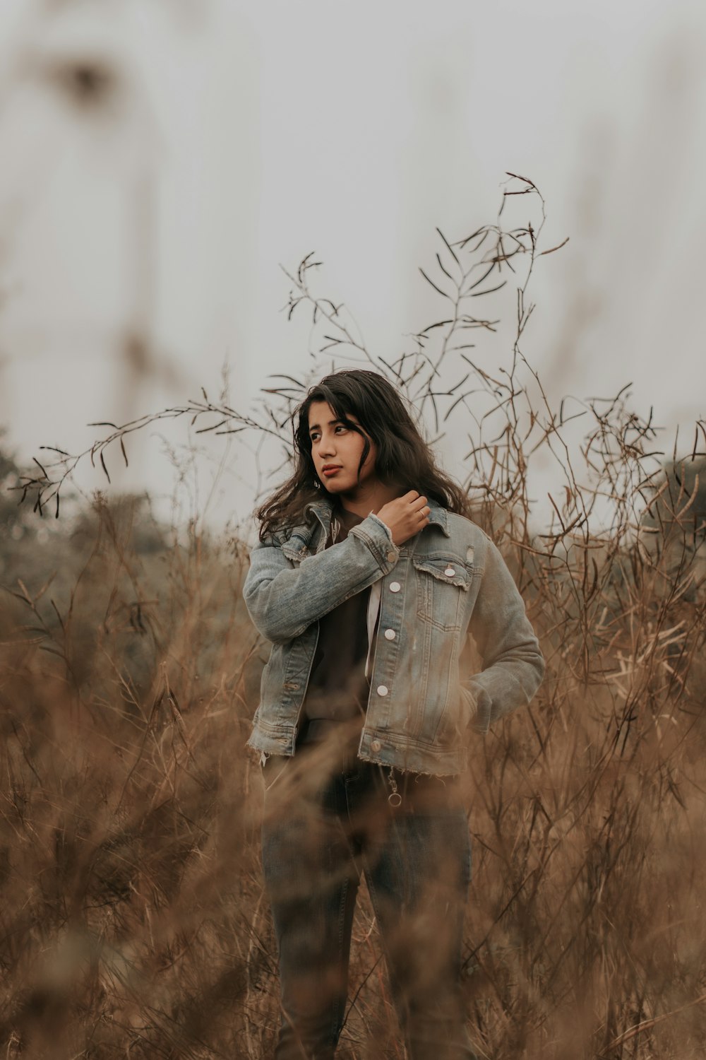 Donna in giacca di jeans grigia in piedi sul campo di erba marrone durante il giorno