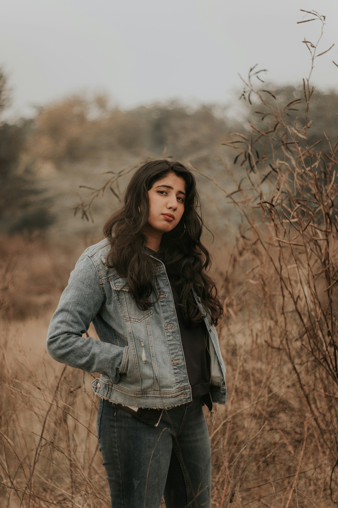 woman in gray denim jacket standing on brown grass field during daytime