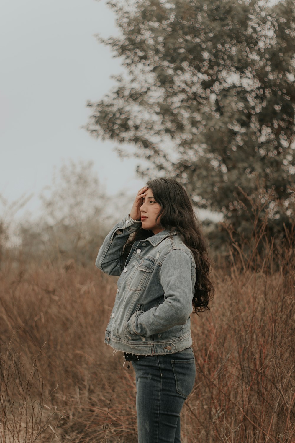 woman in gray denim jacket standing near trees during daytime