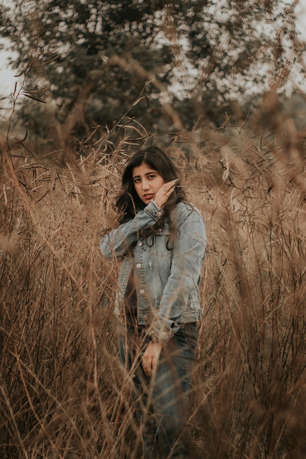 mulher na jaqueta jeans azul que está em pé no campo marrom da grama durante o dia