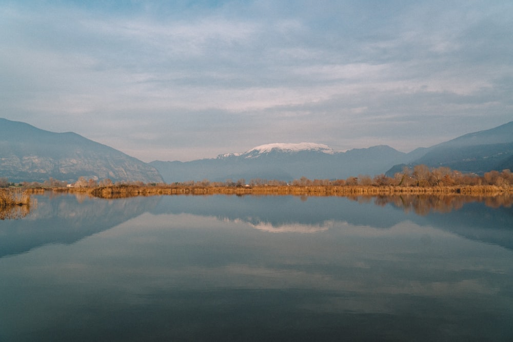 lake near mountain under white sky during daytime