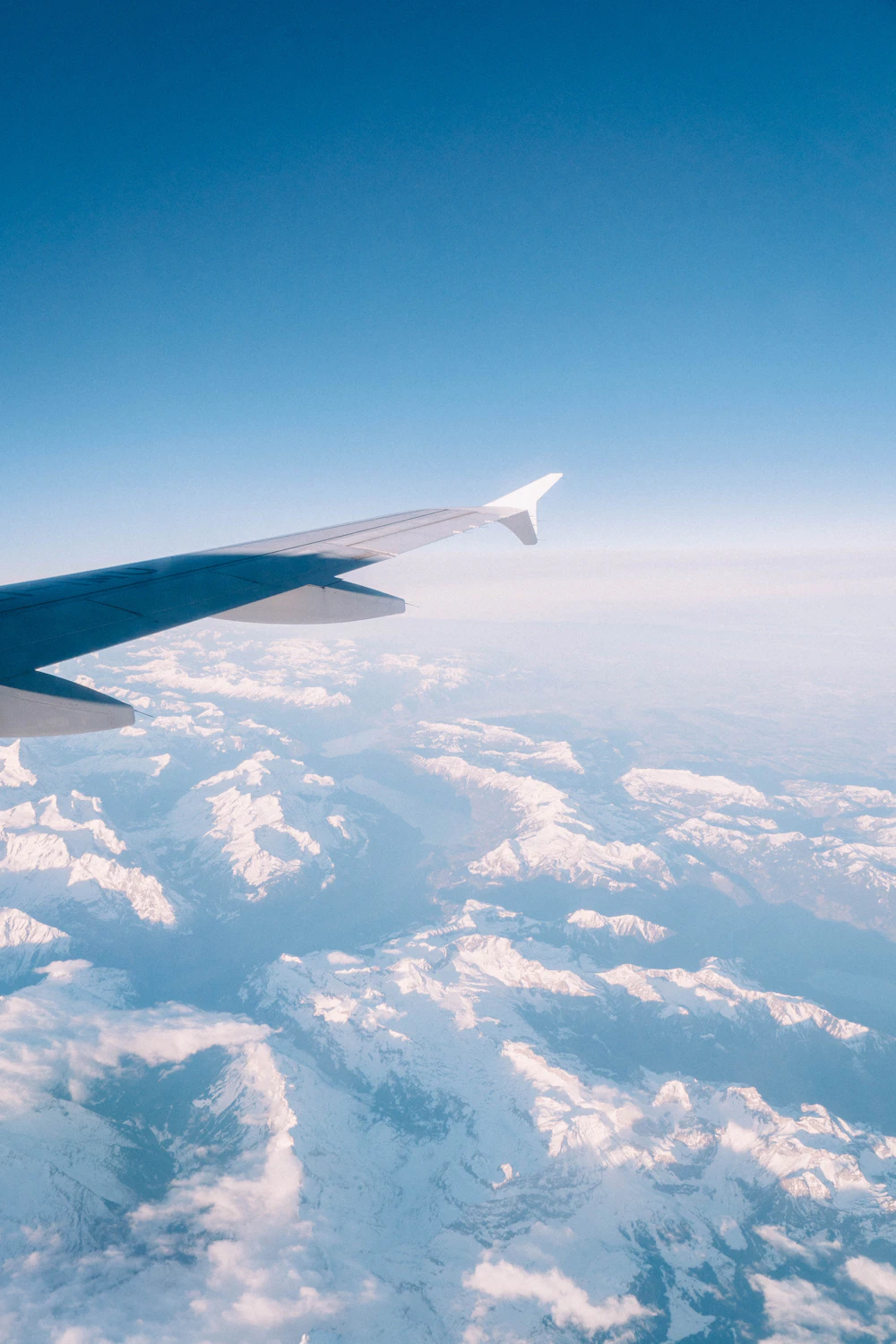 Aircraft wing above soft clouds and snow-capped mountains