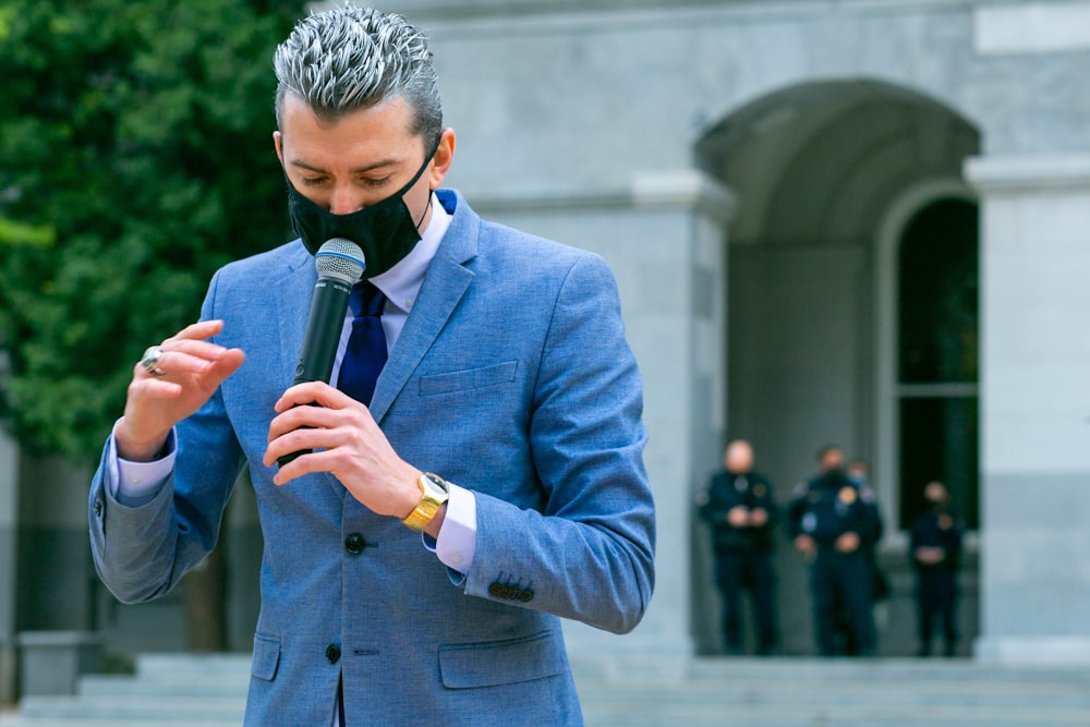 Homme en veste de costume bleue tenant un microphone noir