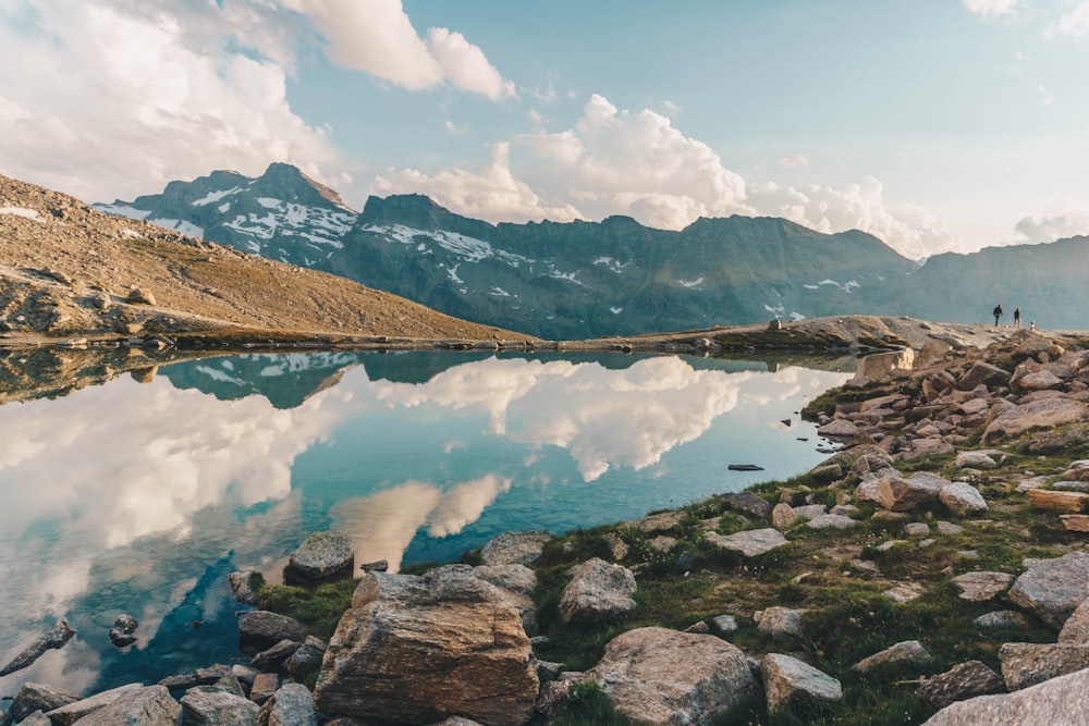 montanhas marrons perto do lago sob nuvens brancas e céu azul durante o dia