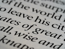 Close-up of printed text in a serif font with words in sharp focus, showing various words in different sizes. The text is black on an off-white background, creating a classic and elegant appearance.
