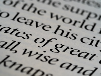 Close-up of printed text in a serif font with words in sharp focus, showing various words in different sizes. The text is black on an off-white background, creating a classic and elegant appearance.