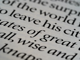 Close-up of printed text in a serif font with words in sharp focus, showing various words in different sizes. The text is black on an off-white background, creating a classic and elegant appearance.