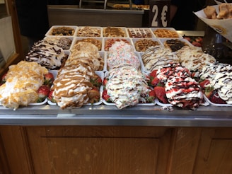 An assortment of waffles topped with various syrups, whipped cream, and strawberries is displayed. There are different toppings like chocolate drizzle and colorful sprinkles, creating an inviting and appetizing presentation.
