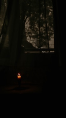 A softly lit room corner featuring a lit domovsviečka candle casting warm shadows.