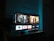 A television screen displaying a user interface with popular streaming service apps including Netflix, Sky, Apple TV, Prime Video, and others. The screen also shows images from movies or shows above the apps. The room is dimly lit with a potted plant visible on the side.