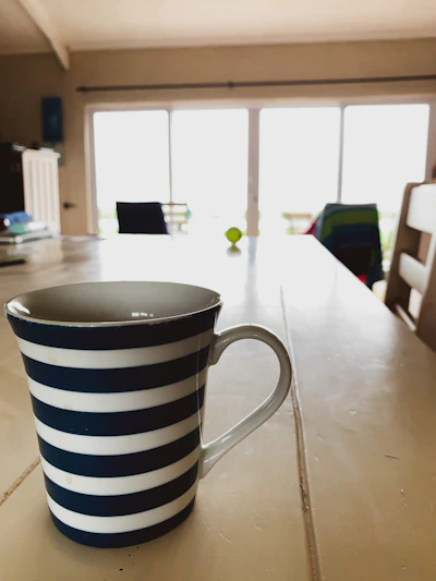 A vibrant hand-thrown stoneware mug in bright turquoise and sunny yellow resting on a cozy wooden table near a window.