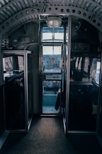 A vintage cockpit interior with metal and glass paneling, featuring an array of dials, gauges, and switches. The cockpit is dimly lit, highlighting the intricate details of the controls and the structure of the cabin.