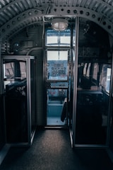 A vintage cockpit interior with metal and glass paneling, featuring an array of dials, gauges, and switches. The cockpit is dimly lit, highlighting the intricate details of the controls and the structure of the cabin.