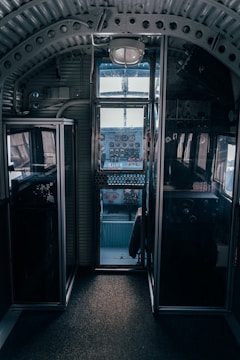 A vintage cockpit interior with metal and glass paneling, featuring an array of dials, gauges, and switches. The cockpit is dimly lit, highlighting the intricate details of the controls and the structure of the cabin.