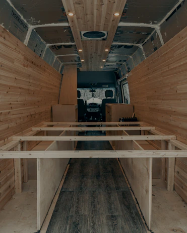 A skilled craftsman fitting wooden panels inside a motor caravan under warm workshop lighting.