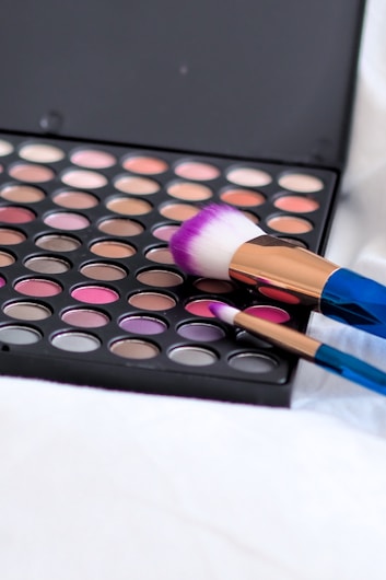 An open makeup palette featuring a wide array of colorful eyeshadow shades alongside two makeup brushes with vibrant bristles.