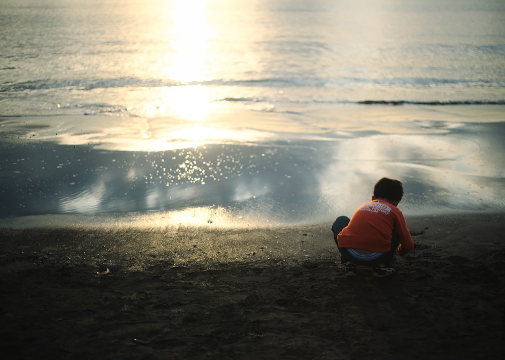 man in red shirt sitting on seashore during daytime