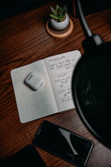 A microphone with headphones on a wooden desk surrounded by notes and a laptop