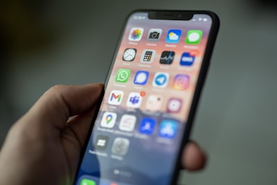 A hand holding a smartphone displaying a home screen with various app icons like WhatsApp, Camera, Calendar, and Gmail. The screen is brightly lit, showcasing a colorful background, and the apps are arranged in a grid pattern.