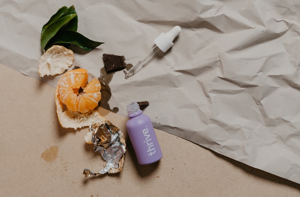 a bottle of lip polish next to a broken orange