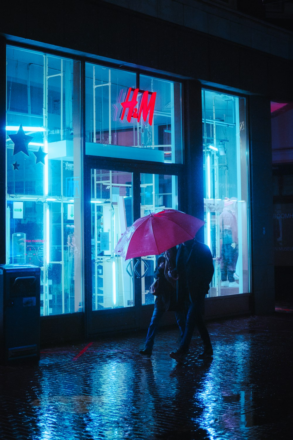 夜間に歩道を歩く傘を持った黒いジャケットを着た人物