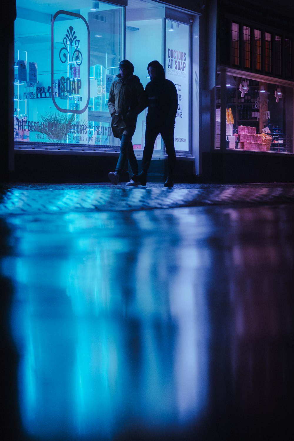 uomo in giacca nera che cammina sul marciapiede durante la notte