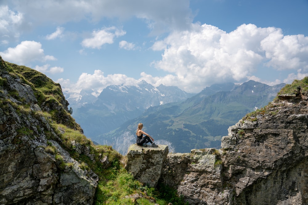 woman in black shirt sitting on rock mountain during daytime