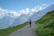 Smiling woman walking on a scenic mountain path with a backpack.