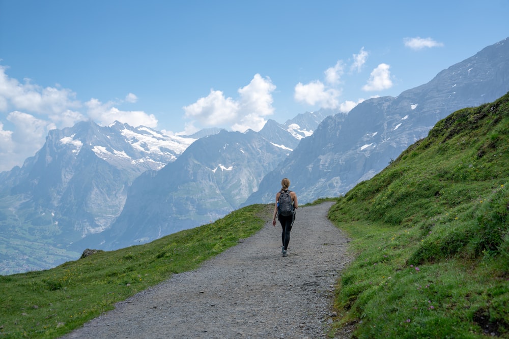 Frau in schwarzer Jacke geht tagsüber auf einem Weg in der Nähe von Bergen spazieren
