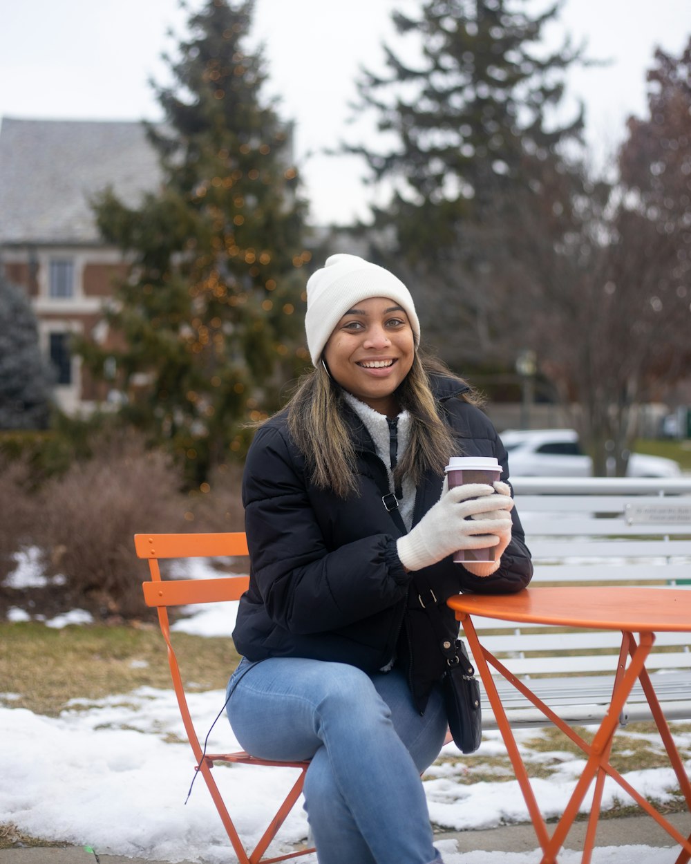 woman in black jacket and blue denim jeans sitting on brown wooden bench during daytime