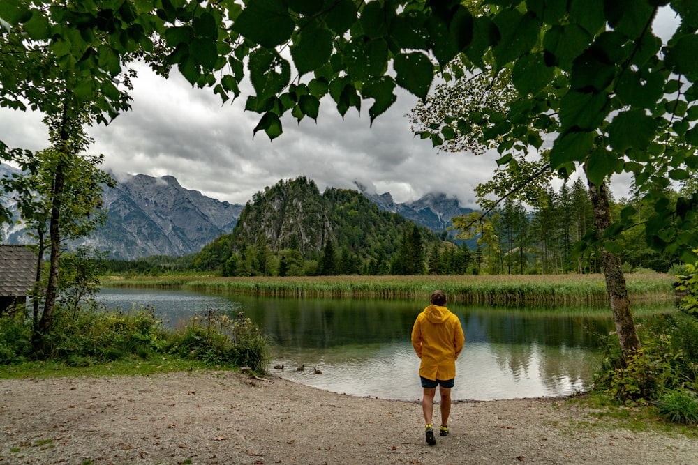 man in yellow jacket and brown shorts standing near lake during daytime