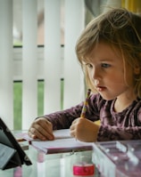 girl in purple and black long sleeve shirt holding black pen writing on white paper