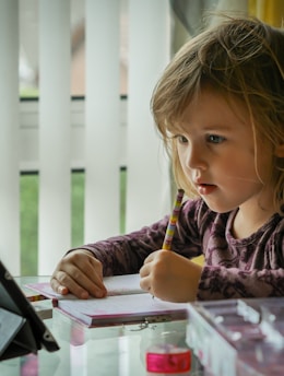 girl in purple and black long sleeve shirt holding black pen writing on white paper