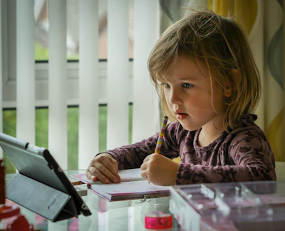 A smiling child writing in a notebook, surrounded by colorful educational materials.