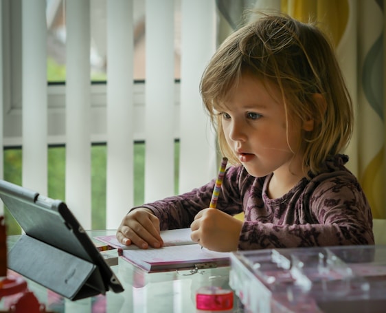 A cheerful child practicing handwriting with colorful pencils and lined paper.