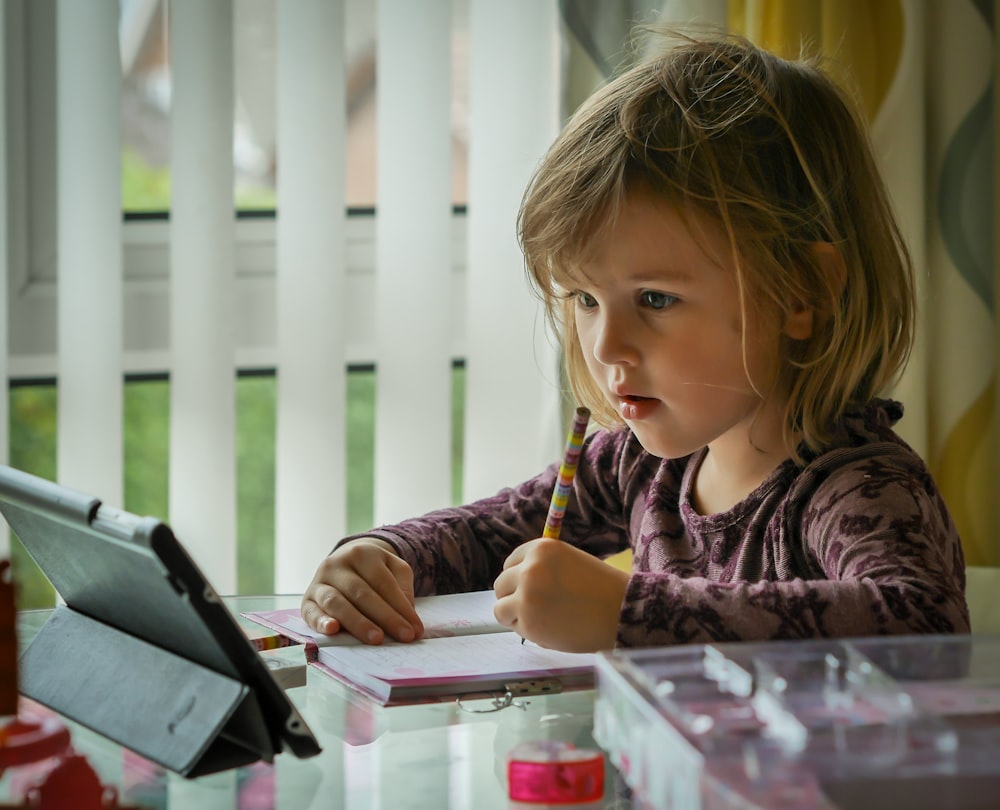 menina na camisa de manga comprida roxa e preta segurando a caneta preta escrevendo no papel branco