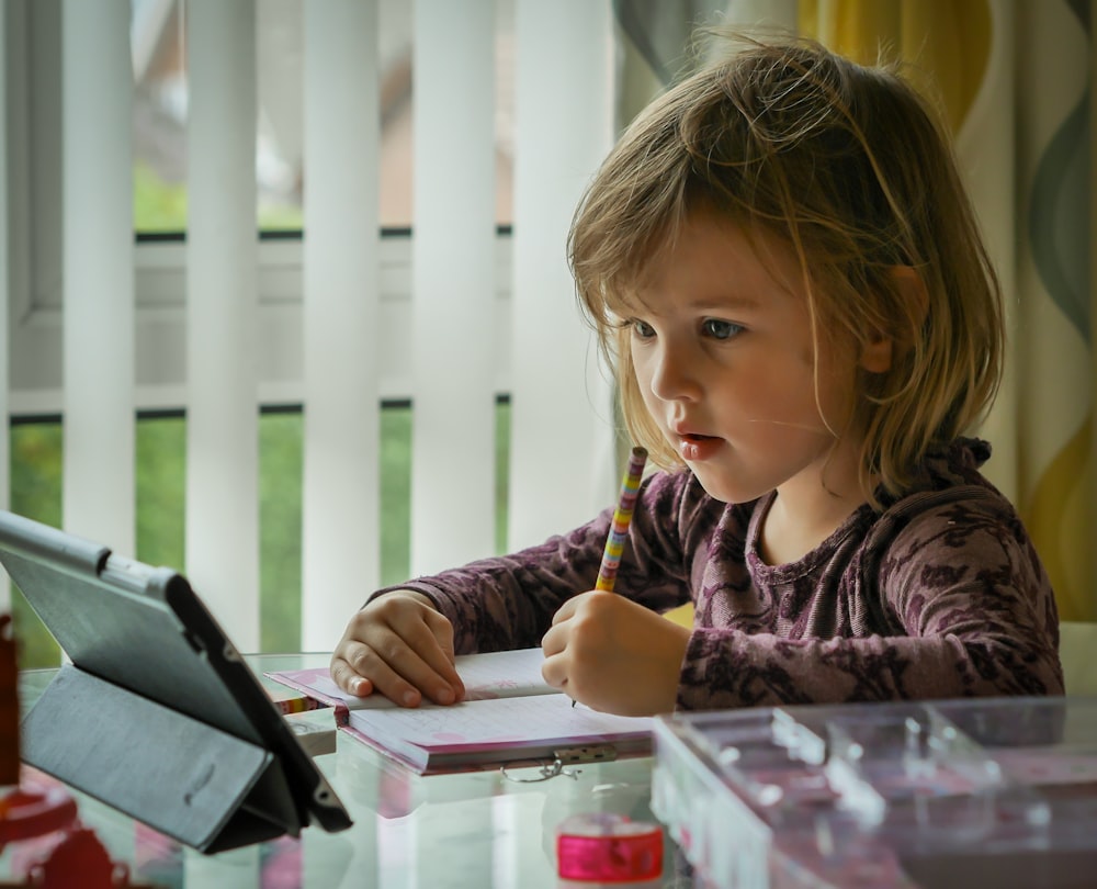 girl in purple and black long sleeve shirt holding black pen writing on white paper