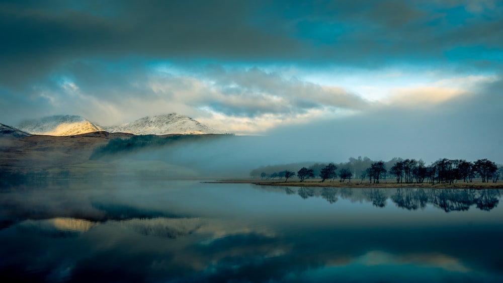 body of water near mountain under cloudy sky during daytime