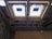 The image depicts the interior ceiling of a building under construction. There are wooden beams and a partial view of the roof structure. Two rectangular window installations are visible.