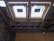 The image depicts the interior ceiling of a building under construction. There are wooden beams and a partial view of the roof structure. Two rectangular window installations are visible.