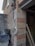 A construction site with exposed brickwork and utility wires coiled against a building wall. Various building materials such as bricks and stone blocks are present, along with a black tarp covering some items. A ladder is visible inside the structure.