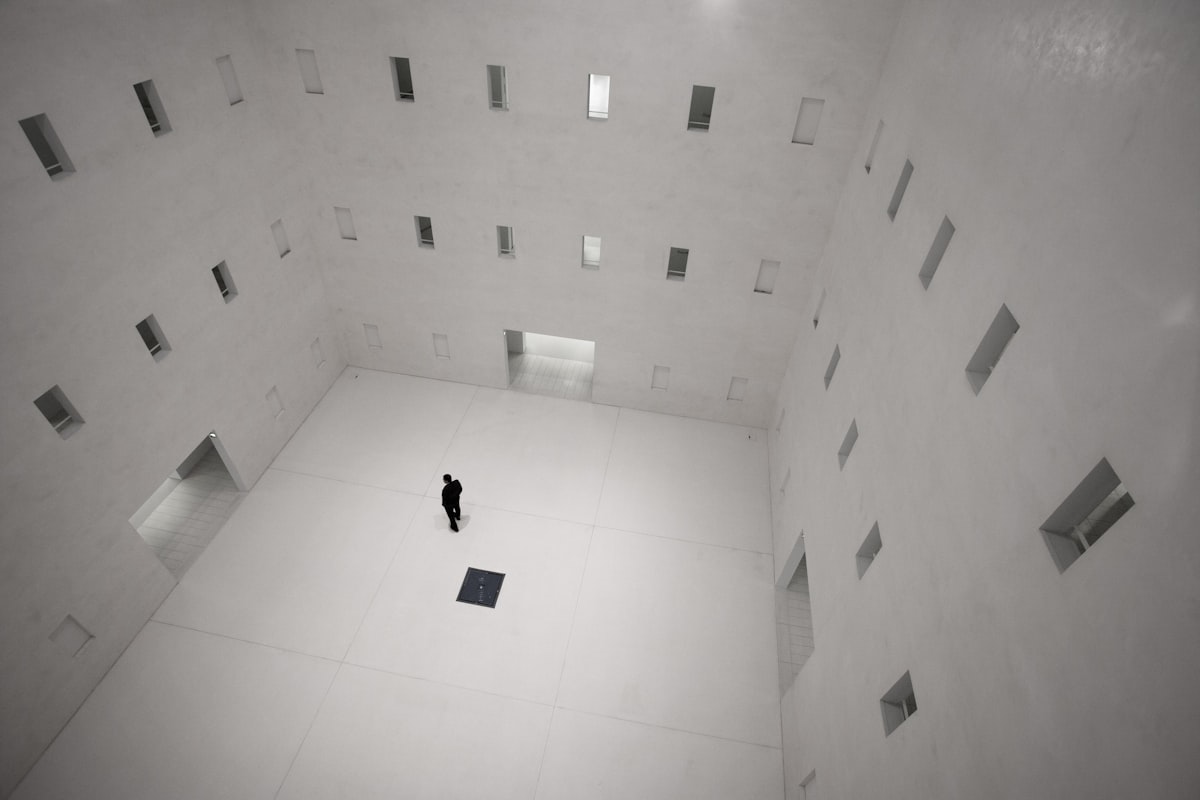 A dark sillouhette of a person in a white room with 3 visible exits and several windows