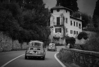 A charming vintage car winding through the lush English countryside, framed by historic stone cottages.